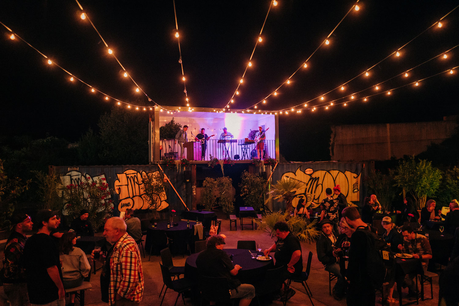 Drei Container, die aufeinander gestellt sind, mit einer Band und langen Lichterketten in Richtung Kamera