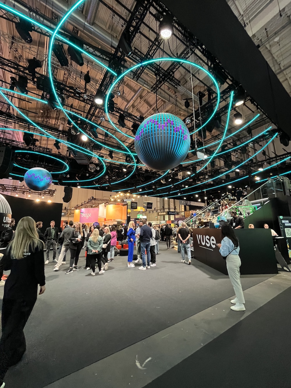 Stand von Yuse mit dynamischer LED-Deckenkonstruktion in Wellenform, leuchtende Kugelobjekte, Besucher*innen im Austausch.
