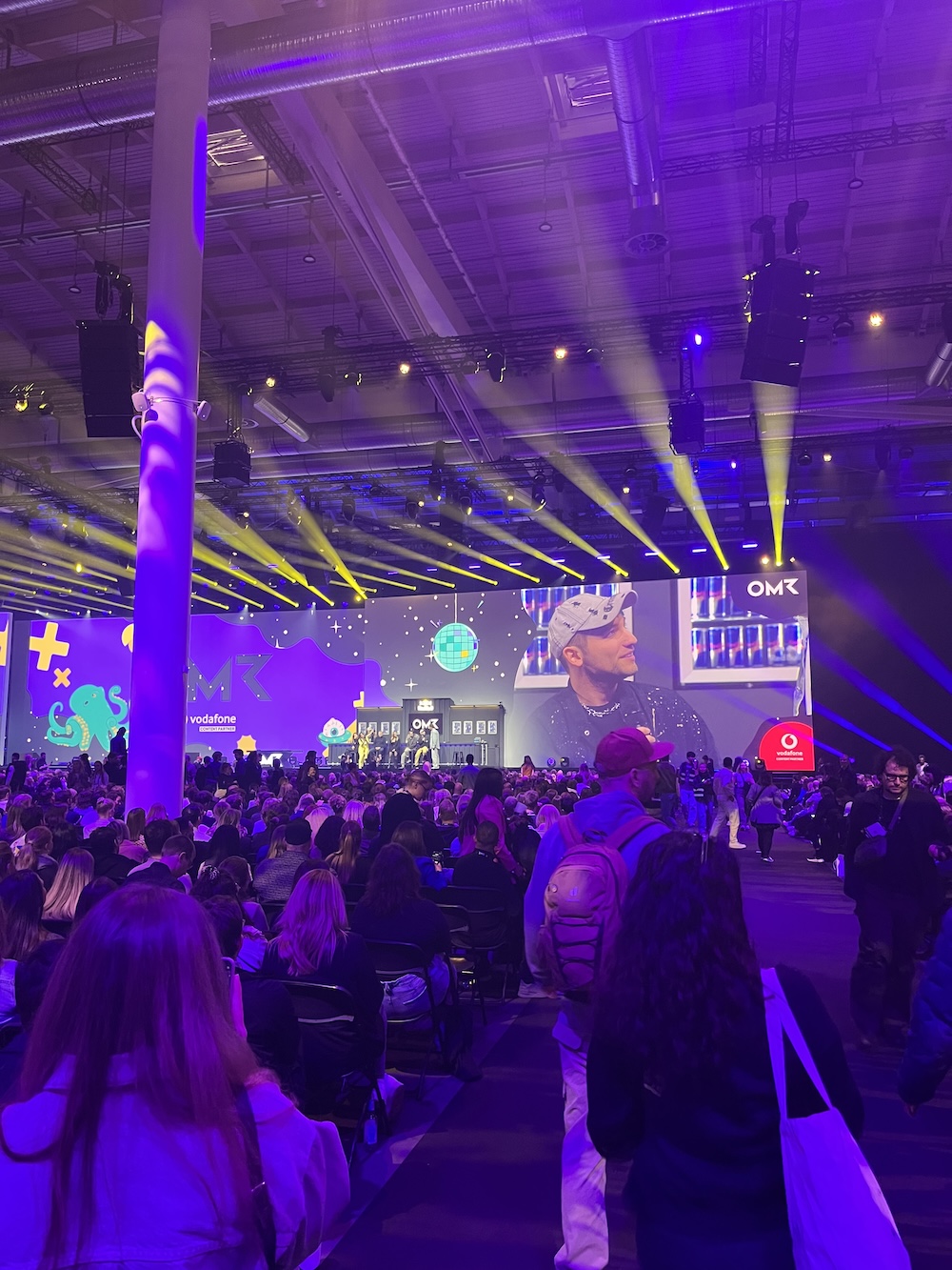 Große Main Stage der OMR mit lila und gelbem Lichtdesign, ein Speaker wird auf einer Leinwand gezeigt, viele Zuschauer*innen im Raum.
