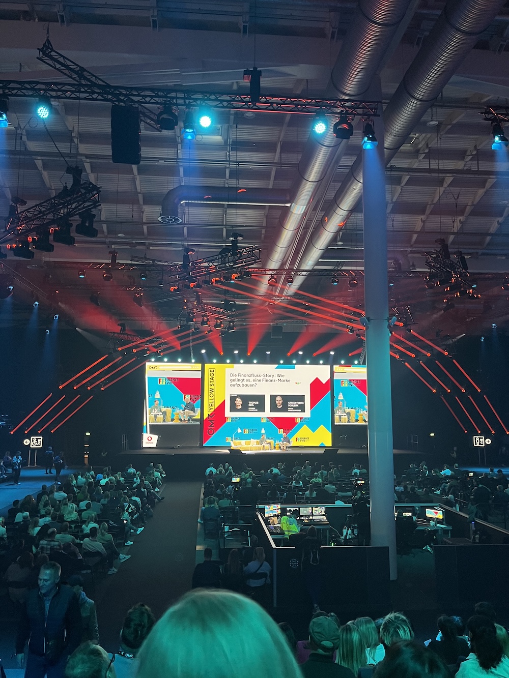 Publikum vor der OMR Yellow Stage, auf der über den Aufbau der Marke „Finanzfluss“ diskutiert wird, rotes und blaues Licht prägt die Atmosphäre.