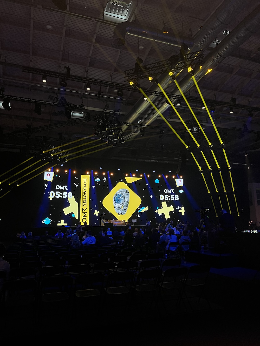 Blick auf die OMR Yellow Stage kurz vor Beginn einer Session, gelbe Lichtstrahlen und Countdown-Anzeige, viele leere Sitzplätze im Vordergrund.