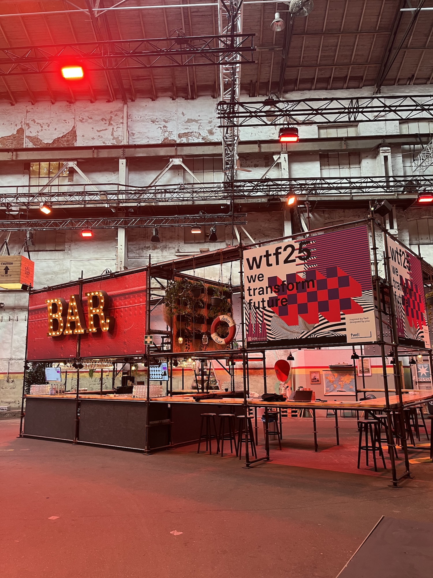 Stylishly staged bar inside the event hall featuring a red glowing “BAR” sign and wtf25 branding. The industrial vibe is enhanced by scaffolding, lighting, and decorative elements.
