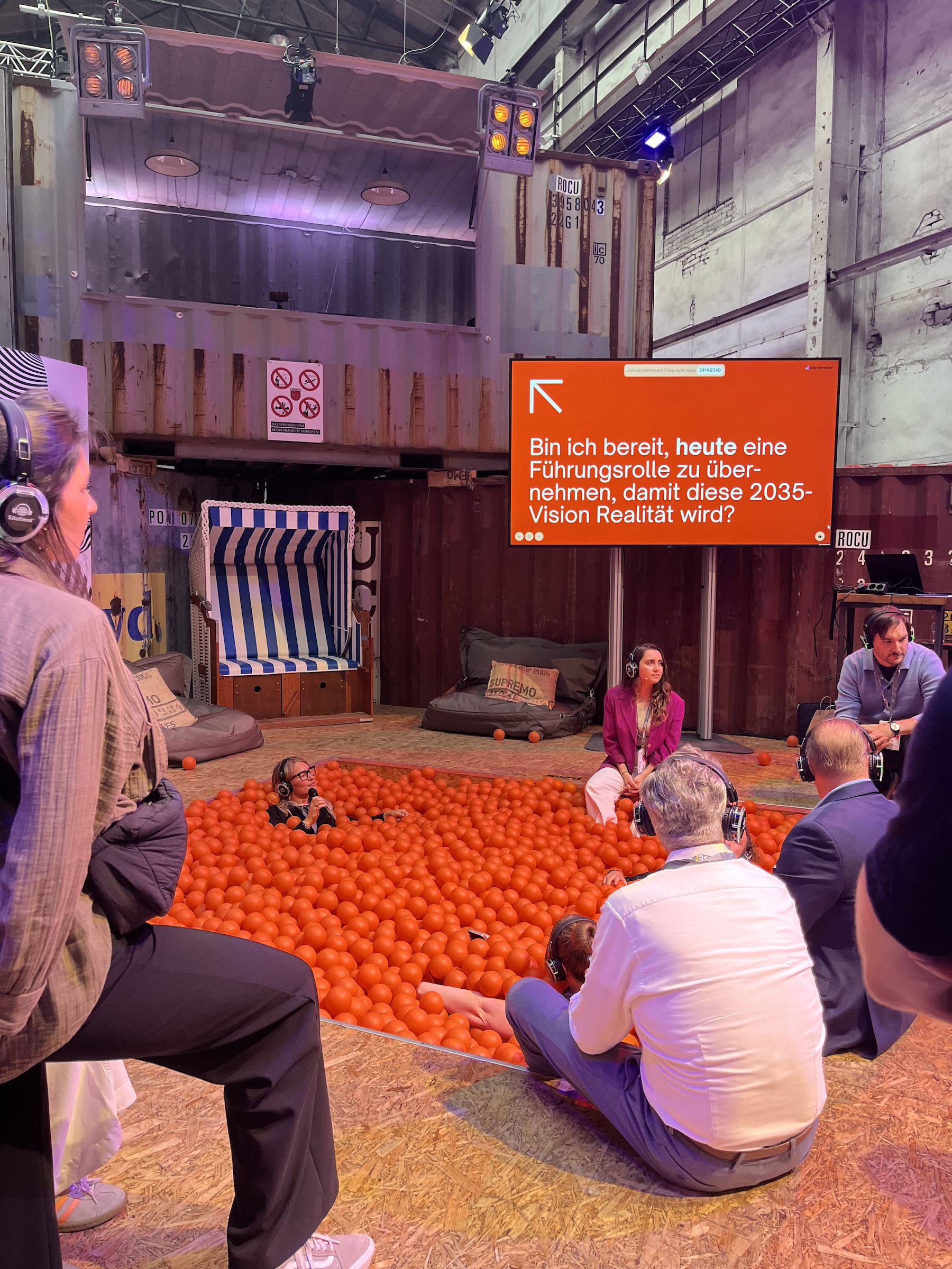 Small discussion round with headphones in the wtf25 “interaction area,” some participants seated in the orange ball pit. On screen: “Am I ready to take on a leadership role today to make the 2035 vision a reality?”