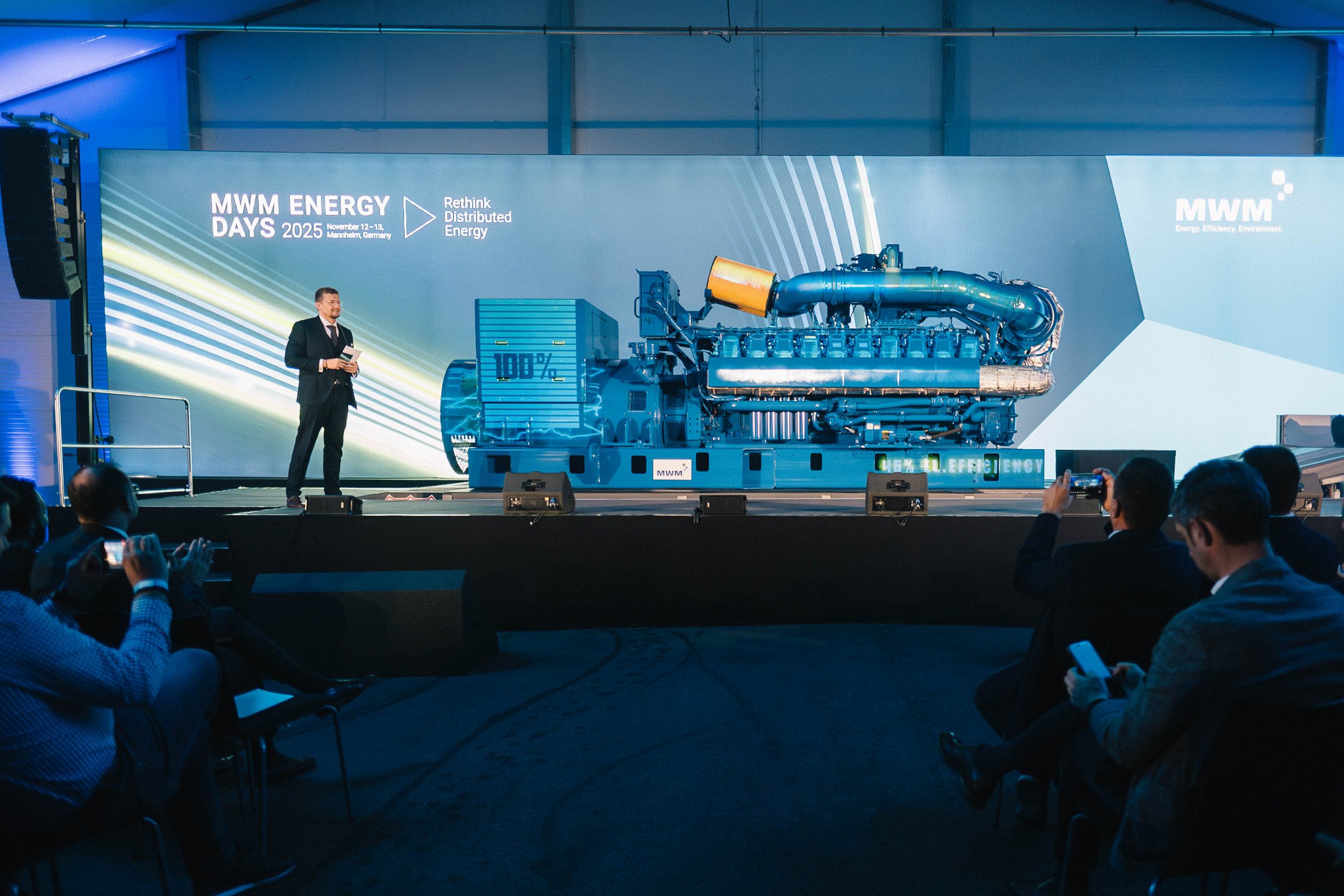 Technological highlight of the event: Unveiling of a large blue engine on stage at MWM ENERGY DAYS 2025. A moderator addresses the audience.