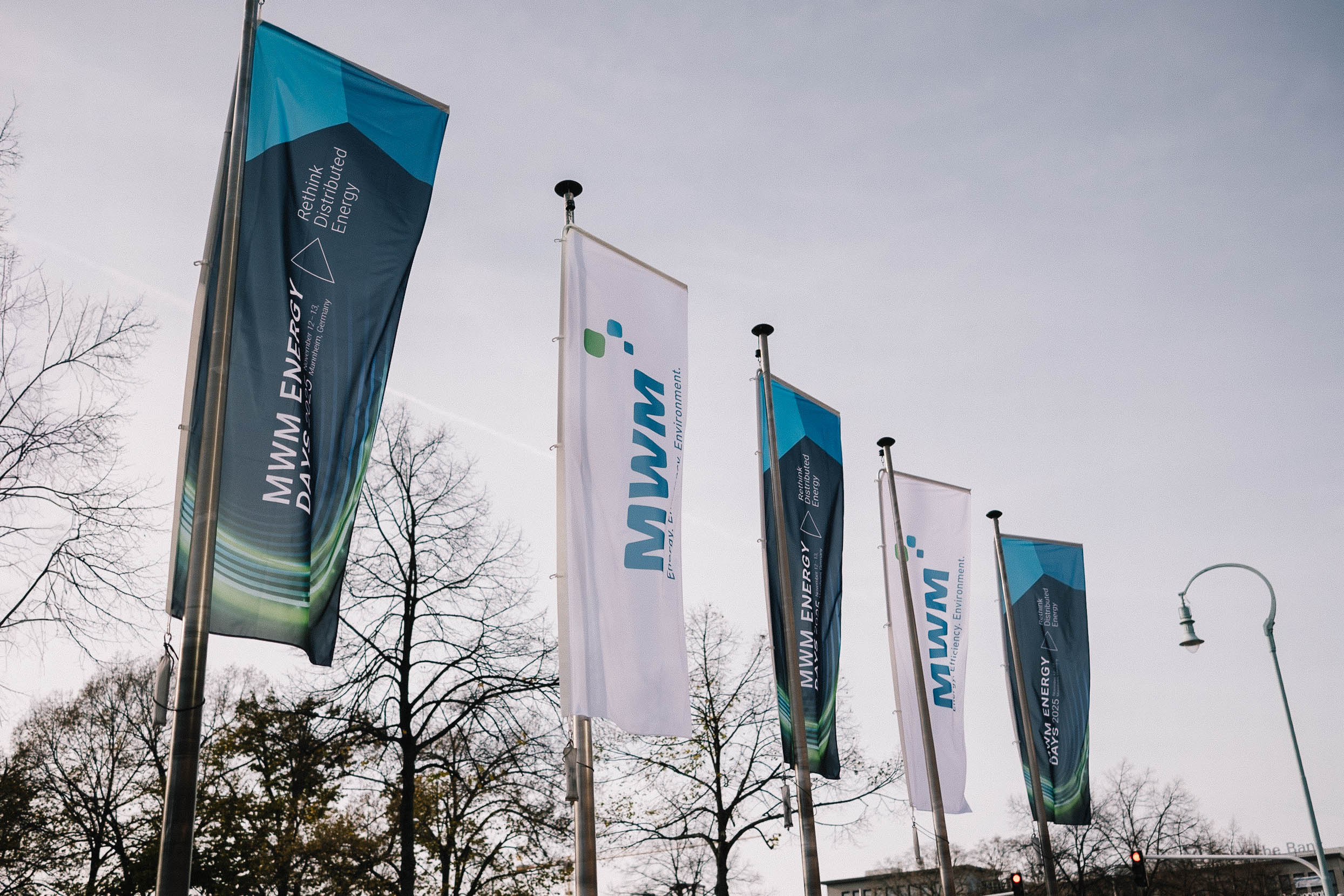 Outdoor shot of waving event flags for MWM ENERGY DAYS 2025. The flags feature the slogans “Rethink Distributed Energy” and the MWM logo.