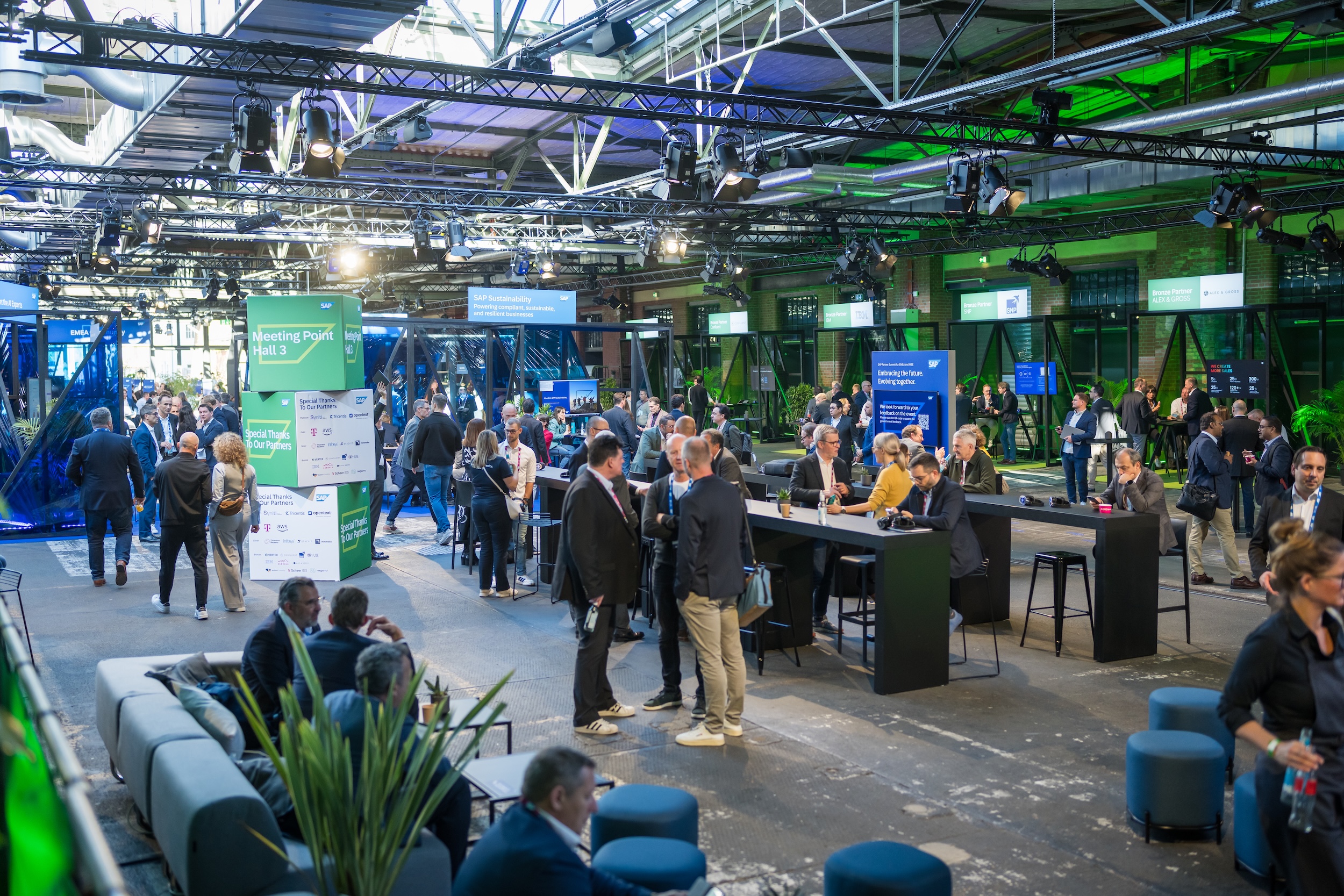Networking area at the SAP Partner Summit with numerous visitors gathered around high tables and lounge seating. Central signage reads “Meeting Point Hall 3” with partner logos.
